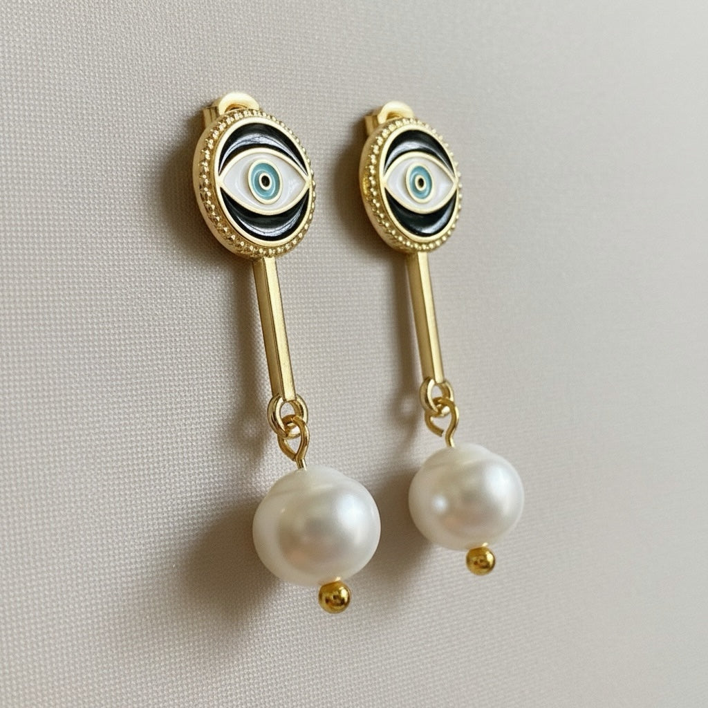 Riri Bespoke Jewelry gold-tone drop earrings featuring evil eye motifs with black enamel and lustrous faux pearl drops.