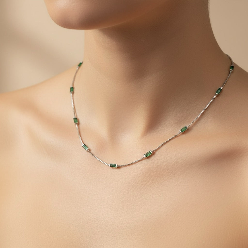 Riri Bespoke Jewelry emerald baguette station necklace on a silver-tone chain worn around a woman's neck.