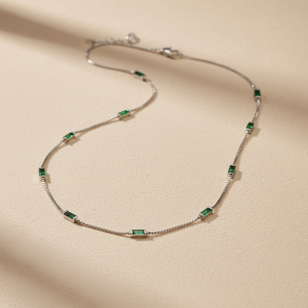 Riri Bespoke Jewelry elegant station necklace with emerald baguette stones on a shimmering silver-tone chain.