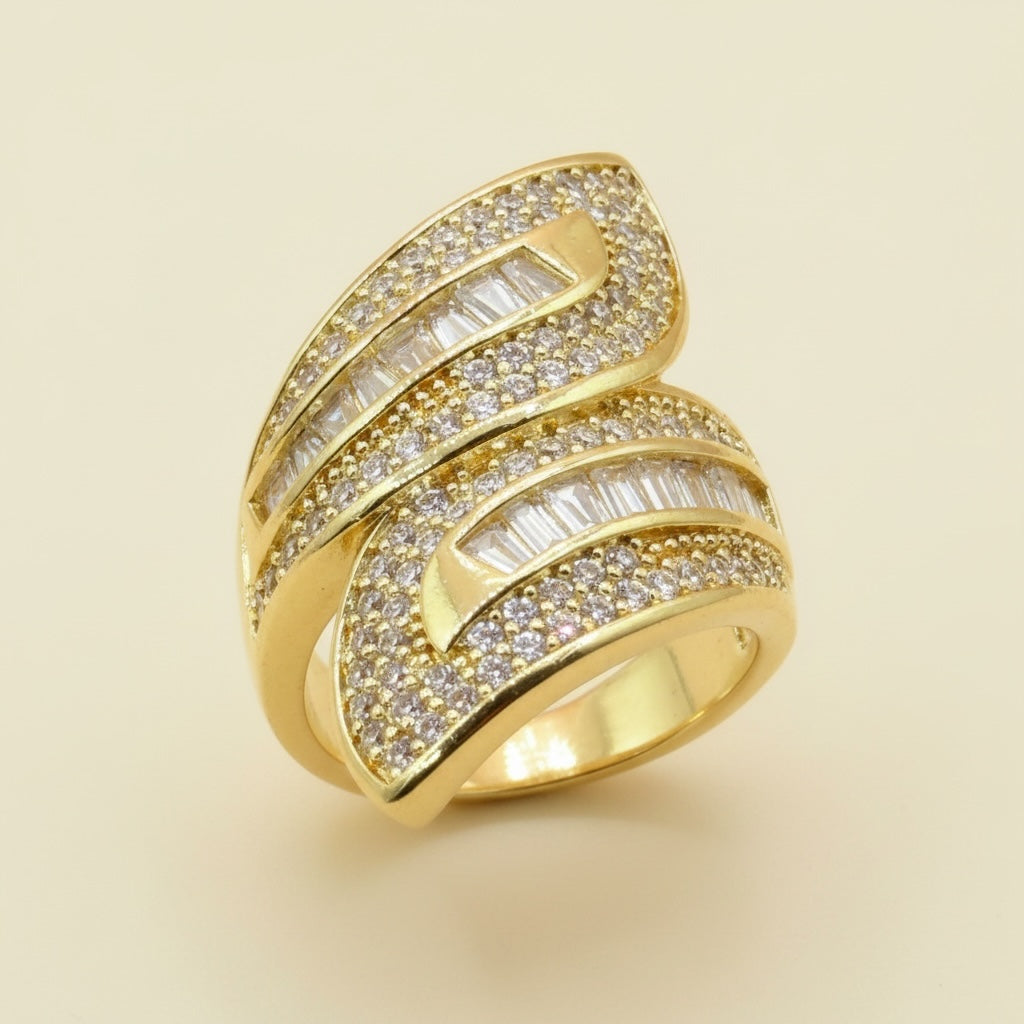 Riri Bespoke Jewelry gold-tone bypass statement ring with pave crystals and baguette-cut stones on a neutral background